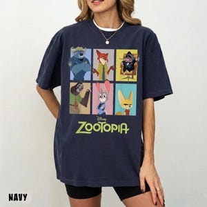 May include: Navy blue Zootopia t-shirt featuring a grid of character illustrations. The shirt includes images of a police officer, fox, mouse, sloth, rabbit, and fox. The word "Zootopia" is printed in green below the images.
