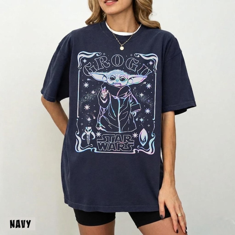 May include: Navy blue t-shirt featuring a graphic of Grogu from Star Wars. The design includes the text "GROGU" and "STAR WARS" in a decorative frame. The shirt is a relaxed fit.