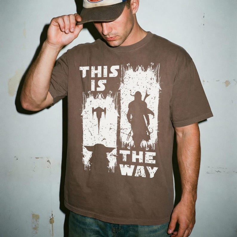 May include: Brown t-shirt with the text "THIS IS THE WAY" in white, along with silhouette images of a character and a creature. The shirt is a solid brown color.