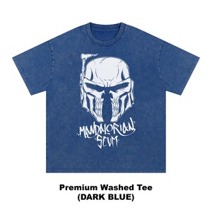 Pu&ograve; includere: T-shirt blu scuro con grafica bianca di un casco a forma di teschio e la scritta "Mandalorian Scum". La maglietta &egrave; una t-shirt lavata di alta qualit&agrave;. Il testo "Premium Washed Tee (DARK BLUE)" &egrave; in basso.