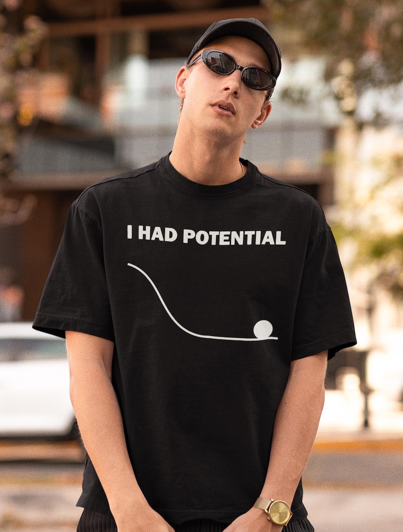 May include: Black t-shirt with the white text "I HAD POTENTIAL" and a white graphic of a ball rolling down a curved line. The shirt is short-sleeved and worn by a person wearing a black cap and sunglasses.