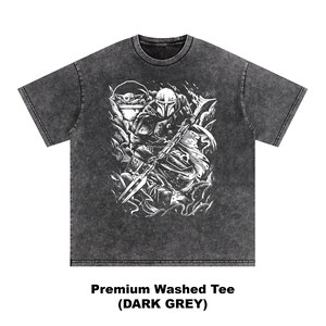 Puede incluir: Camiseta lavada premium gris oscuro con un gr&aacute;fico blanco de un personaje con casco y lanza, y una peque&ntilde;a criatura. El texto "Premium Washed Tee (DARK GREY)" est&aacute; impreso en la parte inferior.