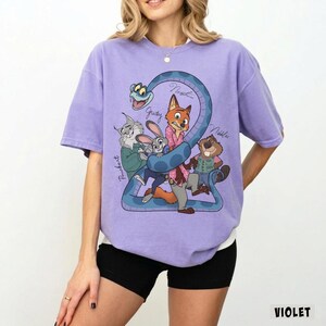 May include: Violet-colored t-shirt featuring a cartoon graphic of characters from a movie. The design includes a blue snake and several animal characters, with names written above them. The word "VIOLET" is printed in the bottom right corner.