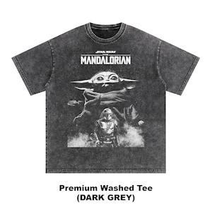 May include: Dark grey, washed t-shirt featuring a graphic from The Mandalorian. The design includes the show's logo, Grogu, and the Mandalorian. The text at the bottom reads "Premium Washed Tee (DARK GREY)".