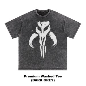 May include: Dark grey, washed t-shirt featuring a white graphic design. The design is a stylized, symmetrical emblem with curved horns and vertical lines. The text "Premium Washed Tee (DARK GREY)" is printed below the shirt.