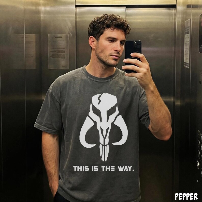 May include: Dark gray t-shirt featuring a white skull design and the text "THIS IS THE WAY." The shirt has a vintage, washed look. The design is centered on the front of the shirt.