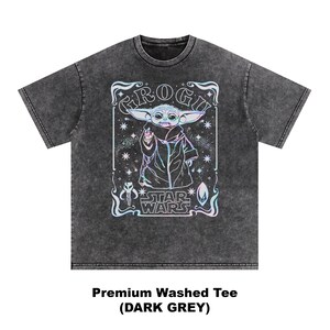 May include: Dark grey t-shirt featuring a Grogu graphic from Star Wars. The design includes Grogu, stars, and the Star Wars logo in a holographic style. The shirt is a premium washed tee.