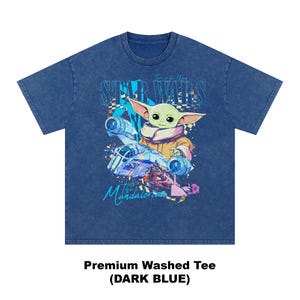 May include: Dark blue premium washed tee featuring a graphic of Grogu from The Mandalorian, with the text "Star Wars" and "The Mandalorian". The graphic includes a spaceship and Grogu in a tan coat. The shirt is a dark blue colour.