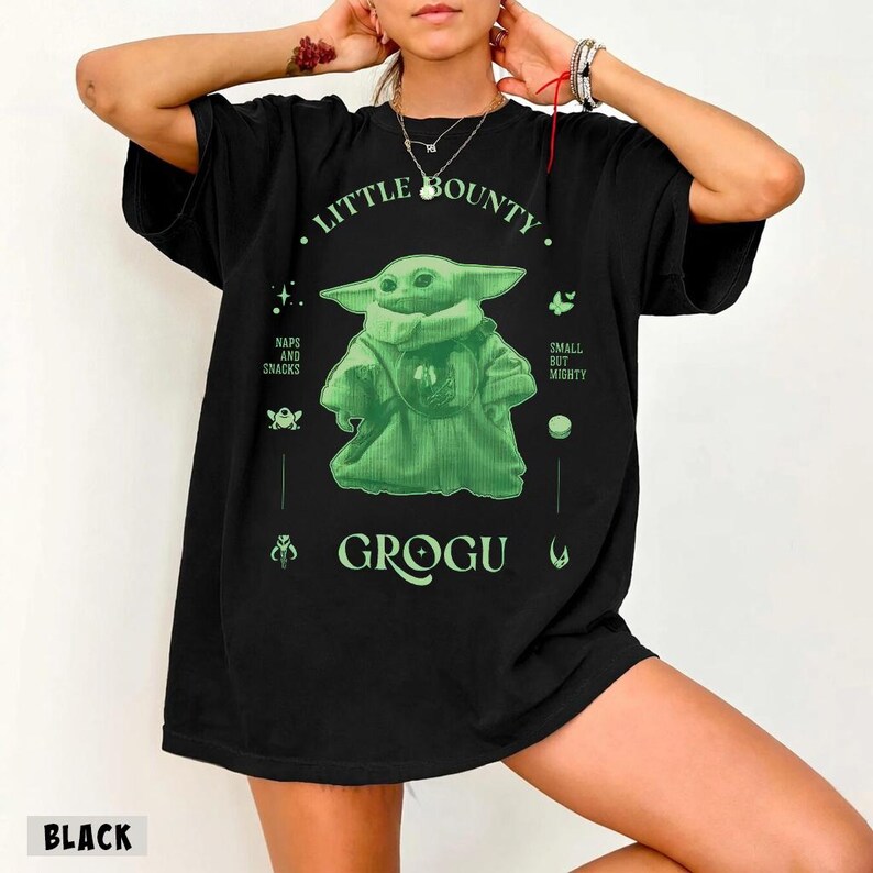 Op de afbeelding: Zwart T-shirt met een groene Grogu-afbeelding en de tekst "Little Bounty". Het ontwerp bevat de zinnen "Naps and Snacks" en "Small but Mighty". Het woord "Grogu" staat onder het personage gedrukt.