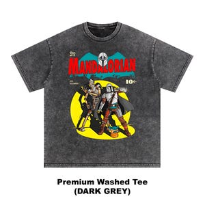 May include: Dark grey premium washed tee featuring a comic book style graphic. The graphic includes the word "MANDALORIAN" in red and teal, with two characters in armor. The shirt also has the text "Clan of 2" and "10&cent;".