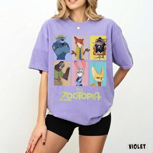 May include: Violet-colored Zootopia t-shirt featuring a grid of character illustrations from the Disney movie. The shirt displays the Zootopia logo in green. The shirt is a short-sleeved, crew neck style.