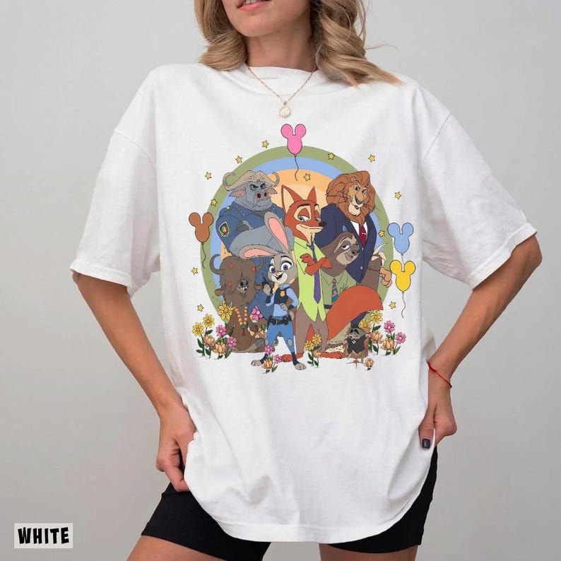 May include: White t-shirt featuring a colorful graphic of characters from a popular animated movie. The design includes a fox, a rabbit, a lion, and other animal characters, surrounded by flowers and stars. The word "WHITE" is printed at the bottom.