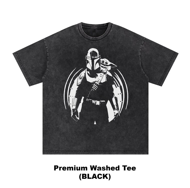 May include: Black washed tee with a white graphic of a Mandalorian character and Grogu, inside a circular design. The text "Premium Washed Tee (BLACK)" is printed at the bottom. The shirt has a crew neck and short sleeves.