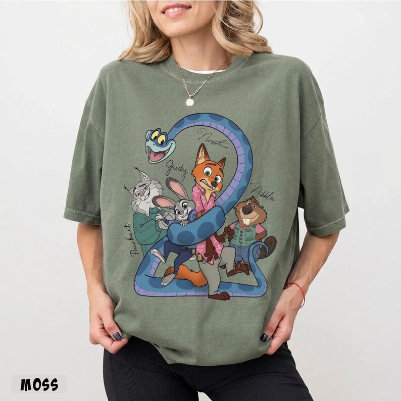 May include: Moss green t-shirt featuring a cartoon graphic of characters from Zootopia, including Judy Hopps and Nick Wilde. The design includes a blue snake and character names. The word "MOSS" is printed at the bottom.