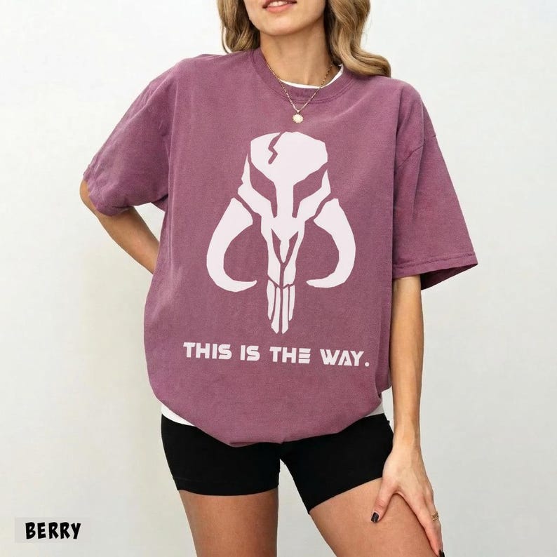 May include: Berry-colored t-shirt featuring a white graphic of a horned skull and the phrase "THIS IS THE WAY." The shirt has a relaxed fit and short sleeves. The text "BERRY" is at the bottom left corner.