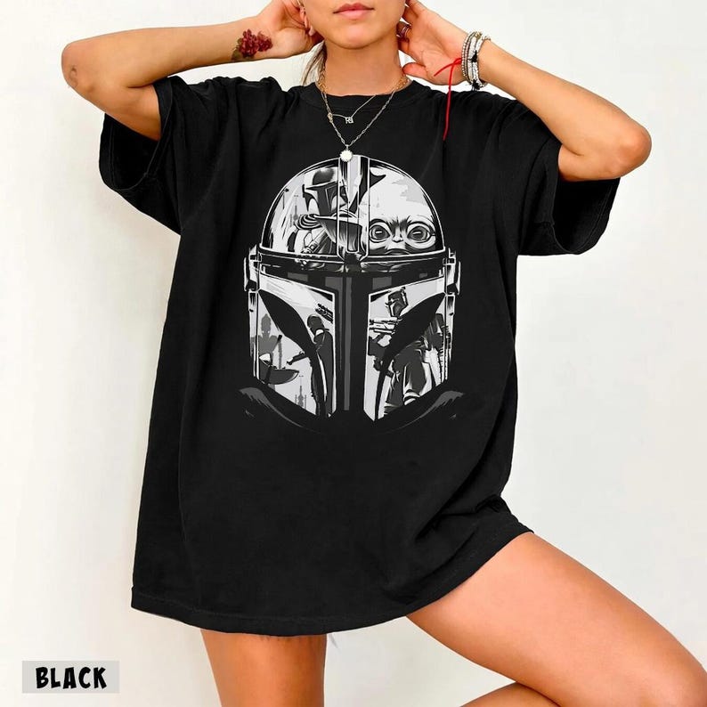 May include: Black t-shirt with a graphic print of The Mandalorian's helmet and Grogu in grey and white. The word "BLACK" is printed at the bottom of the shirt.