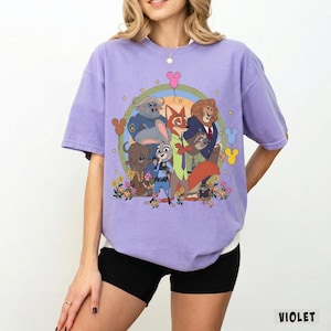May include: Violet-colored t-shirt featuring a colorful graphic of animated animal characters. The design includes a rainbow, balloons, and flowers. The word "VIOLET" is printed in white at the bottom right corner of the shirt.