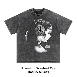 May include: Dark grey t-shirt featuring a black and white portrait of a woman with a headpiece, with the Star Wars logo. The shirt has the text "Premium Washed Tee (DARK GREY)".