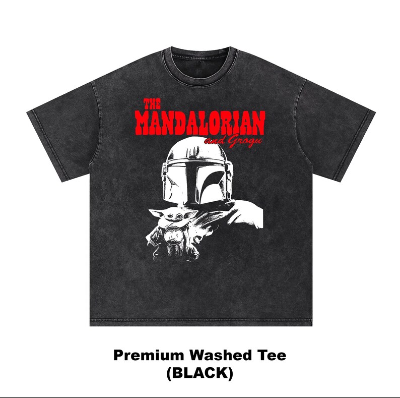 Op de afbeelding: Zwart premium gewassen T-shirt met een afbeelding van The Mandalorian en Grogu. Het ontwerp bevat de helm van de Mandalorian en Grogu in wit, met de tekst "THE MANDALORIAN and Grogu" in rood. De stijl van het shirt is een vintage wassing.