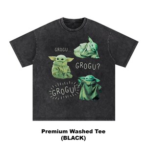 May include: Black washed tee featuring four Grogu illustrations in green. The shirt has the text "GROGU...", "GROGU?", and "GROGU!" in white. The bottom of the shirt reads "Premium Washed Tee (BLACK)".