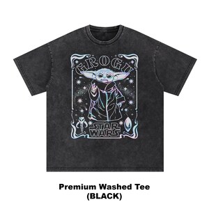May include: Black washed tee featuring a graphic of Grogu from Star Wars. The design includes the text "Grogu" and "Star Wars" with a colorful, holographic effect. The shirt is a premium washed tee.