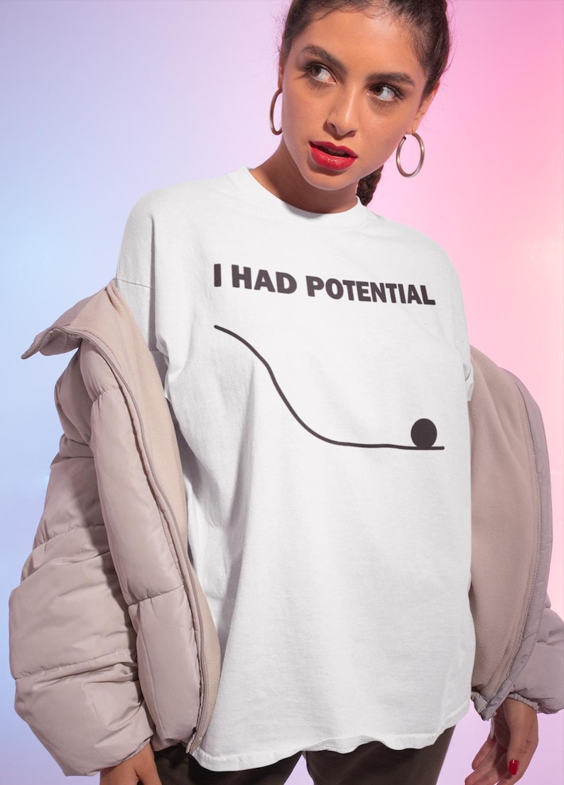 May include: White t-shirt with the text "I HAD POTENTIAL" in black, above a simple black line drawing of a ball rolling down a hill. The shirt is part of a clothing collection.