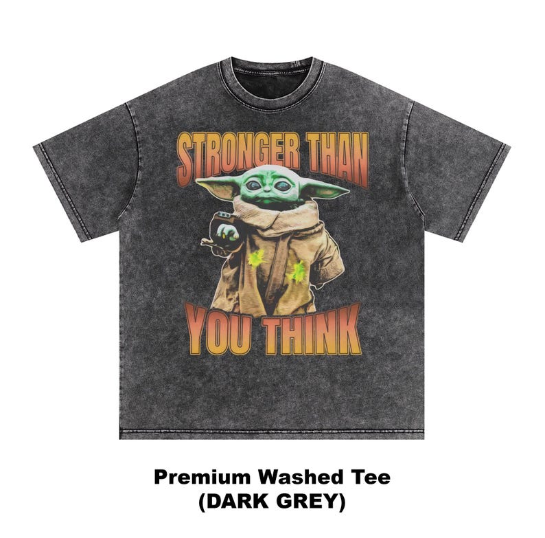 Pode incluir: T-shirt cinza escuro com um gr&aacute;fico de um personagem alien&iacute;gena verde e o texto "STRONGER THAN YOU THINK". A camisa &eacute; uma camiseta lavada premium.