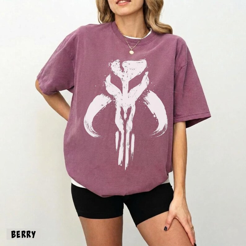 May include: Berry-colored t-shirt featuring a white graphic design. The design is a stylized emblem with curved and vertical lines. The shirt is paired with black shorts. The word "BERRY" is printed at the bottom left of the image.