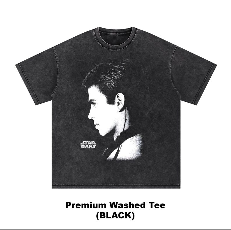 Op de afbeelding: Zwart premium gewassen T-shirt met een zijprofielportret van een persoon. Het Star Wars-logo is zichtbaar aan de linkerkant van het portret. De tekst "Premium Washed Tee (BLACK)" staat onderaan.