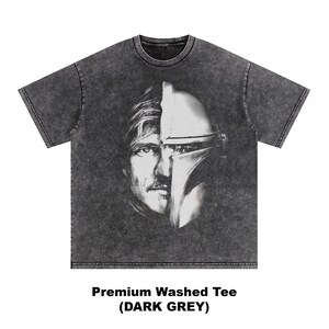 May include: Dark grey washed tee featuring a split face design of a man and a Mandalorian helmet. The graphic is in black and white. The text at the bottom reads "Premium Washed Tee (DARK GREY)".