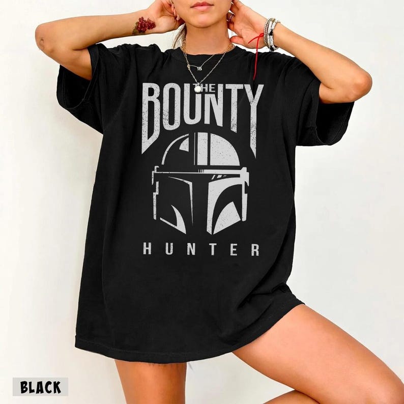 Puede incluir: Camiseta negra con un gr&aacute;fico blanco de un casco y las palabras "THE BOUNTY HUNTER". La palabra "BLACK" est&aacute; impresa en la parte inferior de la camiseta.