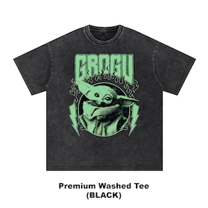 May include: Black washed tee featuring a green graphic of Grogu with the word "GROGU" above. The design includes lightning bolts and flames. The shirt is labeled "Premium Washed Tee (BLACK)".