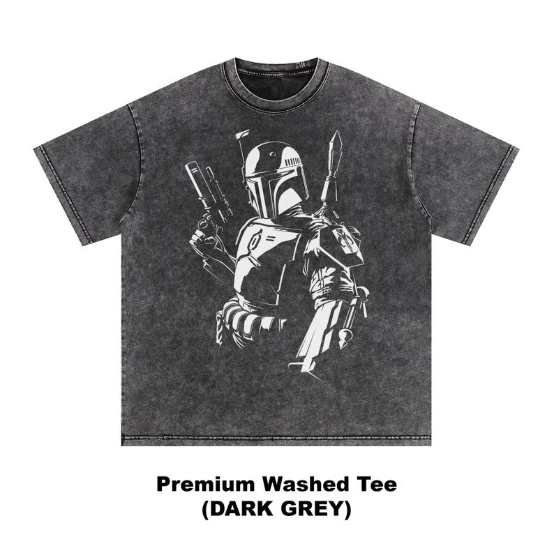 May include: Dark grey washed tee featuring a white graphic of a character with a helmet, holding a blaster and a blade. The text at the bottom reads "Premium Washed Tee (DARK GREY)". The shirt has a crew neck and short sleeves.