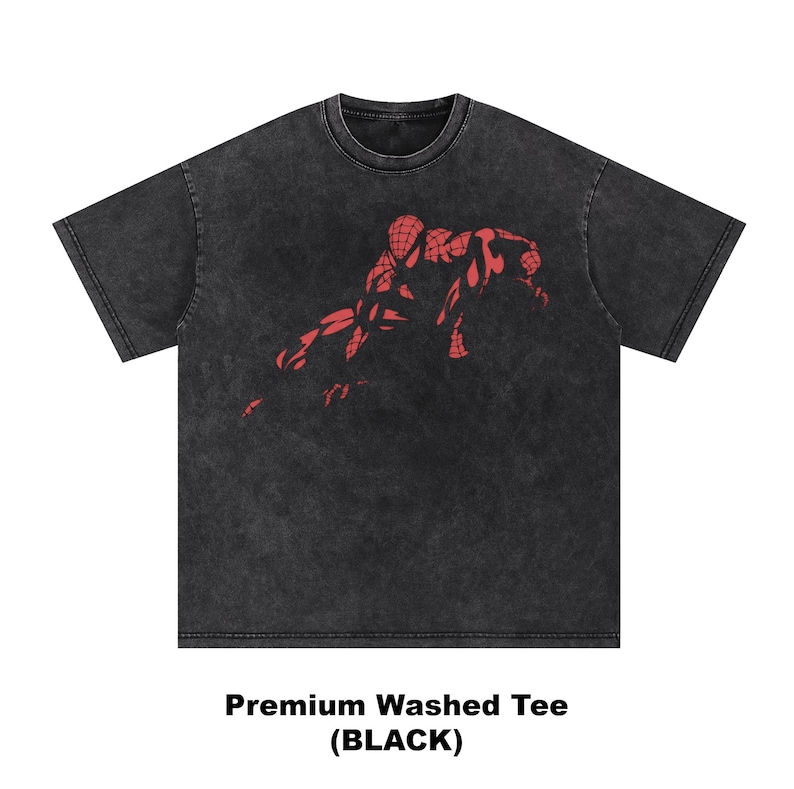 May include: A black short-sleeve t-shirt with a washed, faded texture. The center of the chest features a red graphic illustration of a character in a webbed suit crouched in a dynamic pose. The text Premium Washed Tee (BLACK) appears below.
