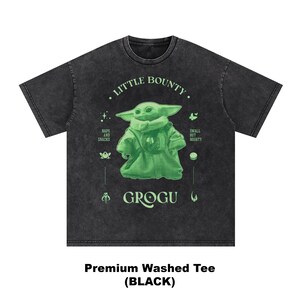 Op de afbeelding: Zwart premium gewassen T-shirt met een groene Grogu-afbeelding en de tekst "Little Bounty". Het ontwerp bevat de zinnen "Naps and Snacks" en "Small but Mighty". Het shirt heeft een donkergrijze kleur.