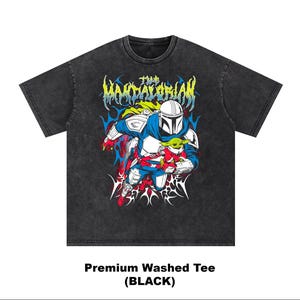 K&ouml;nnte beinhalten: Schwarz gewaschenes T-Shirt mit einer Grafik von The Mandalorian und Grogu. Das Design enth&auml;lt den Text "The Mandalorian" in einer stilisierten Schriftart mit einer Farbpalette aus Blau, Rot, Gelb und Wei&szlig;.
