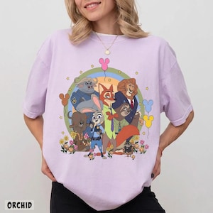 May include: Orchid-colored t-shirt featuring a colorful cartoon graphic of characters from a popular animated movie. The design includes a rainbow, stars, and Mickey Mouse-shaped balloons. The word "ORCHID" is printed at the bottom.