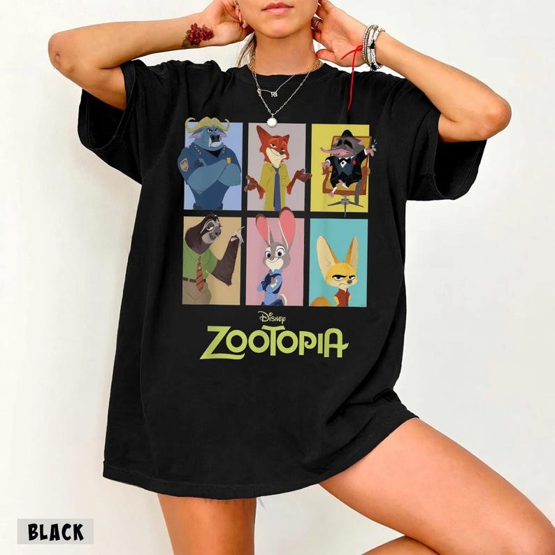 May include: Black t-shirt featuring a colorful graphic of characters from the Disney movie Zootopia. The design includes images of a police officer, a fox, a mouse, a sloth, a rabbit, and a fennec fox. The word "Zootopia" is printed in green.