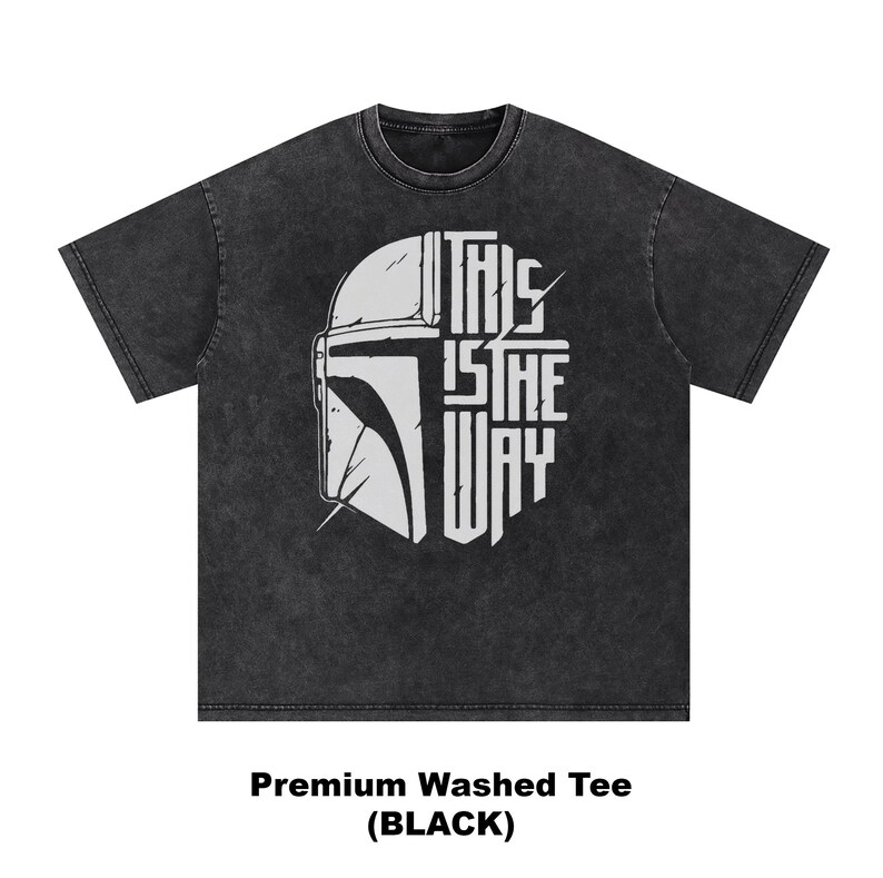 May include: Black washed tee with a white graphic of a helmet and the text "THIS IS THE WAY". The design is centered on the front of the shirt. The shirt is a premium washed tee.