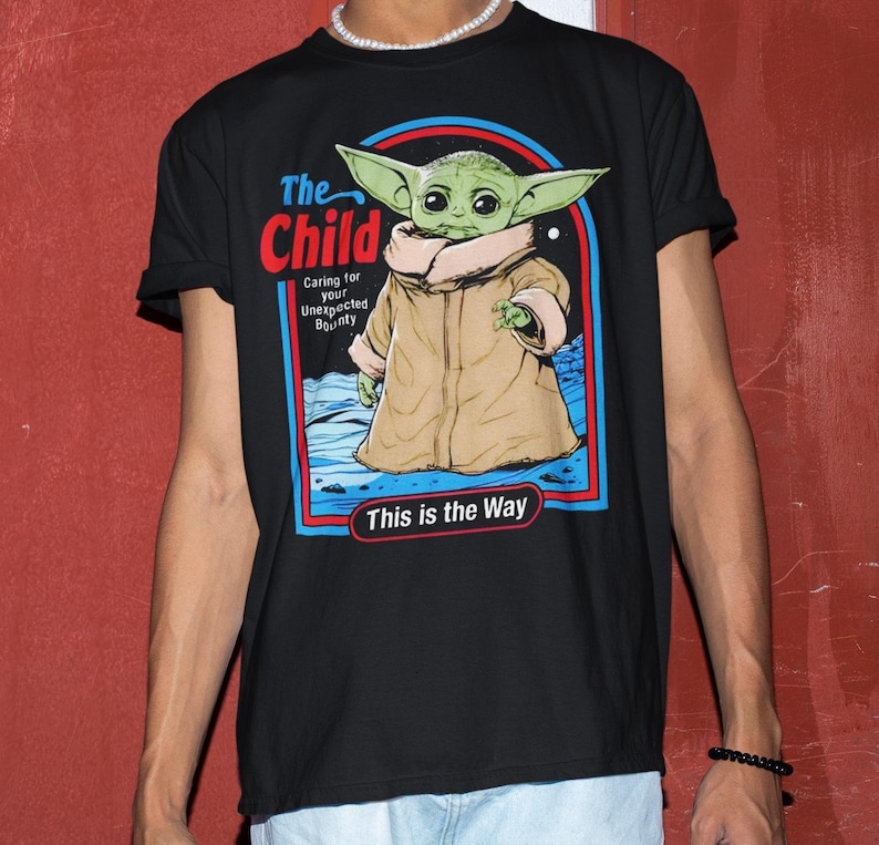 K&ouml;nnte beinhalten: Schwarzes T-Shirt mit einer Grafik von "The Child" aus Star Wars. Das Design enth&auml;lt den Text "The Child" in Rot, "Caring for your Unexpected Bounty" und "This is the Way" in Wei&szlig;.