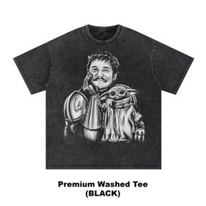 Puede incluir: Camiseta negra lavada con una ilustraci&oacute;n en escala de grises de un hombre y una peque&ntilde;a criatura. El hombre lleva una armadura y la criatura est&aacute; envuelta en una capa. El texto "Premium Washed Tee (BLACK)" est&aacute; en la parte inferior.