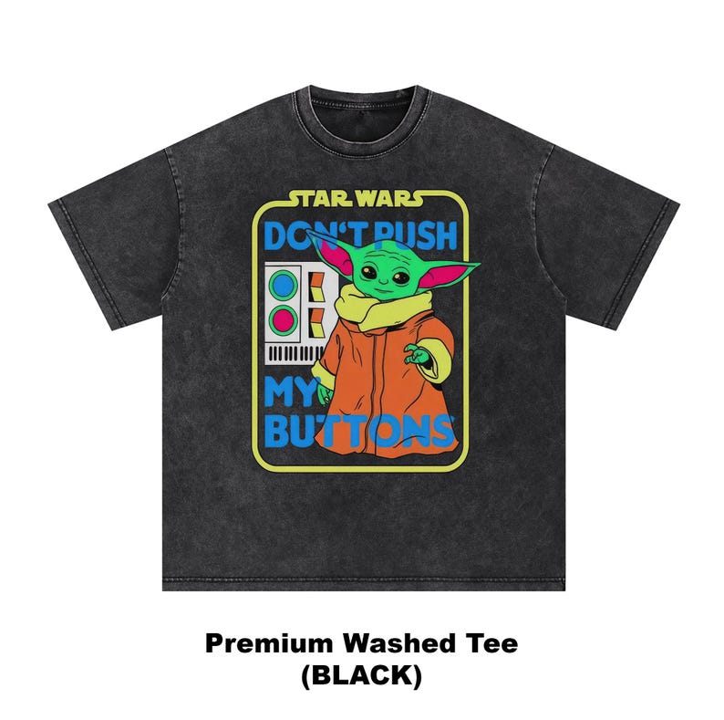 May include: Black washed tee featuring a graphic of Grogu from Star Wars. The design includes the text "DON'T PUSH MY BUTTONS" and a control panel. Grogu is depicted in his orange coat and tan collar. The shirt is a premium washed tee.