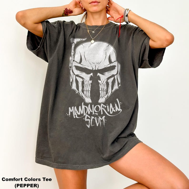 Pu&ograve; includere: T-shirt Comfort Colors grigio scuro con grafica bianca di un casco a forma di teschio e la scritta "MANDALORIAN SCUM". La maglietta oversize ha maniche corte. Il tessuto &egrave; morbido e confortevole.