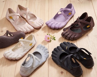 May include: A collection of Vibram five-toe shoes in various colours including light pink, lavender, dark brown, white, grey, and black. Each shoe features a distinct toe-separated design, a cross-strap closure, and a yellow Vibram logo on the side.