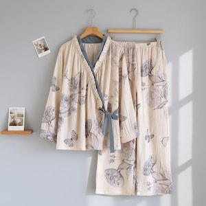 Può includere: Un completo pigiama beige con un motivo floreale e a farfalle. Il set include un top avvolgente con finiture e fiocco blu, e pantaloni abbinati. Il tessuto appare morbido e leggero, adatto per l'abbigliamento da notte.
