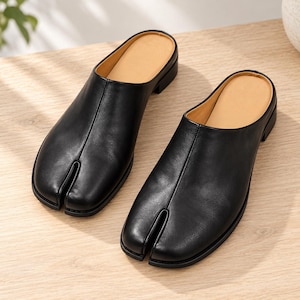 Può includere: Un paio di sabot in pelle nera con un caratteristico design a punta divisa. Queste scarpe senza lacci presentano una tomaia nera liscia, una cucitura centrale sul davanti, un tacco basso a blocco e una fodera interna color beige.