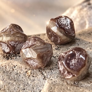 May include: Four small, irregularly shaped beads with a glossy, dark brown and cream-coloured marbled finish. Each bead features a faceted, geometric structure with smooth, reflective surfaces and a distinct horizontal band of lighter cream colour.