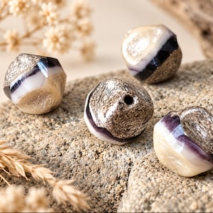 May include: Four faceted beads featuring a layered design with a central band of translucent purple and white stone, flanked by textured metallic silver sections. Each bead has a central hole for stringing, showcasing a mix of smooth and rough finishes.