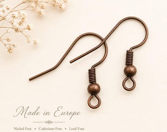 May include: Two antique copper-toned metal earring hooks featuring a coiled wire detail above a small bead and a circular loop at the base. The text Made in Europe, Nickel Free, Cadmium Free, and Lead Free is printed below the earring components.