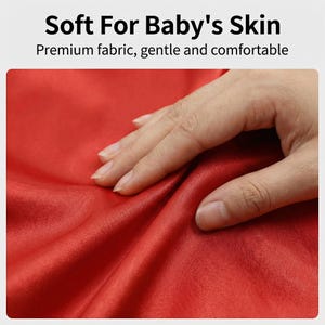 K&ouml;nnte beinhalten: Nahaufnahme eines roten Stoffes mit dem Text "Soft For Baby's Skin" und "Premium fabric, gentle and comfortable". Eine Hand ber&uuml;hrt den Stoff und hebt seine weiche Textur und Qualit&auml;t hervor, ideal f&uuml;r Babys.